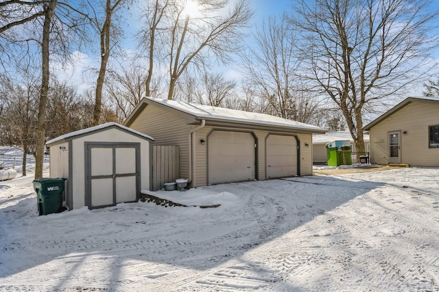 snow covered garage with a storage unit and a detached garage