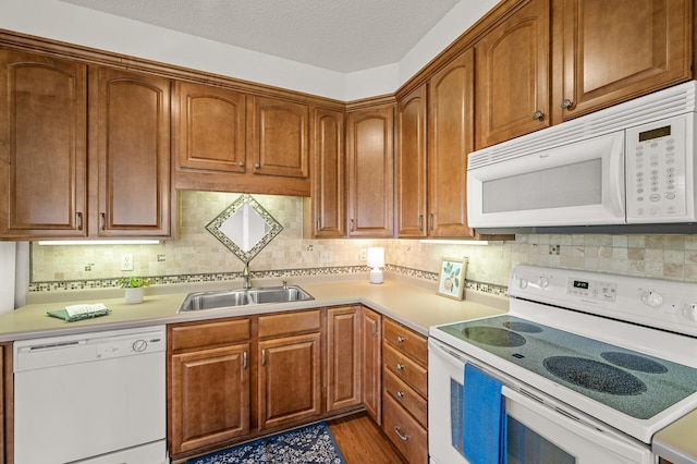 kitchen featuring white appliances, backsplash, a sink, and light countertops
