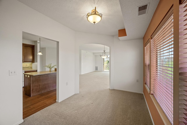 carpeted spare room featuring arched walkways, a textured ceiling, visible vents, and baseboards