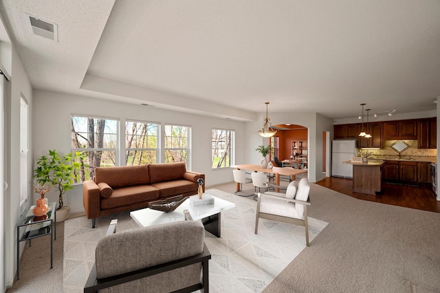 living room featuring visible vents, arched walkways, carpet, and baseboards