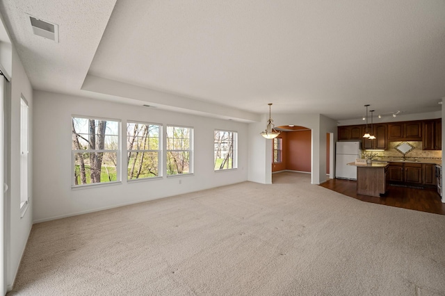 unfurnished living room featuring visible vents, track lighting, dark colored carpet, baseboards, and arched walkways