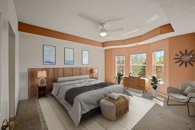 bedroom with baseboards, a ceiling fan, a textured ceiling, and light carpet