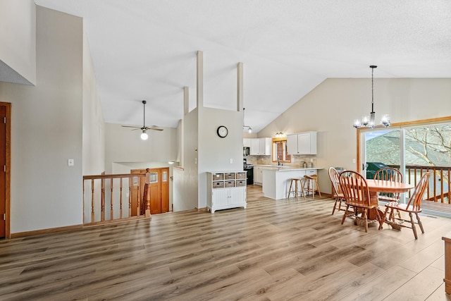 dining room with ceiling fan with notable chandelier, baseboards, light wood finished floors, and high vaulted ceiling