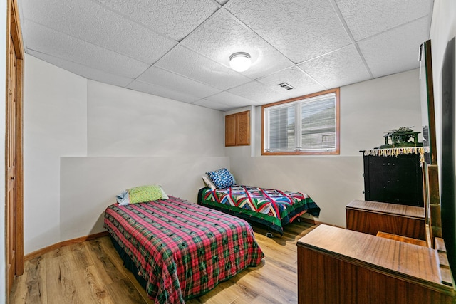 bedroom with a drop ceiling, visible vents, baseboards, and light wood-style flooring