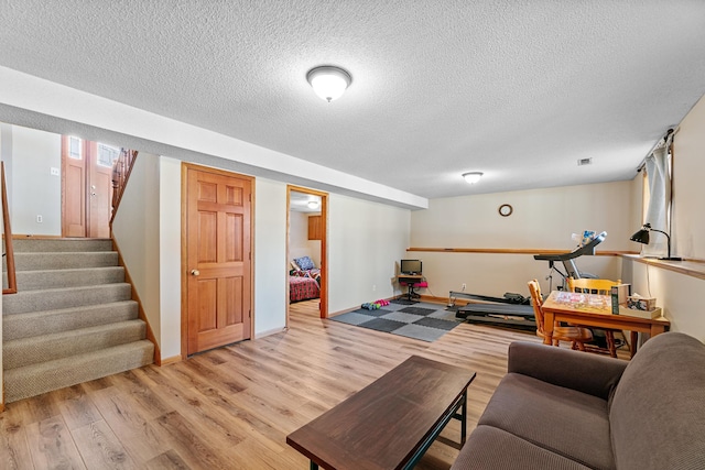 living area with stairs, light wood-style flooring, baseboards, and a textured ceiling