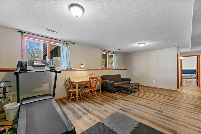 exercise area with a textured ceiling, wood finished floors, visible vents, and baseboards