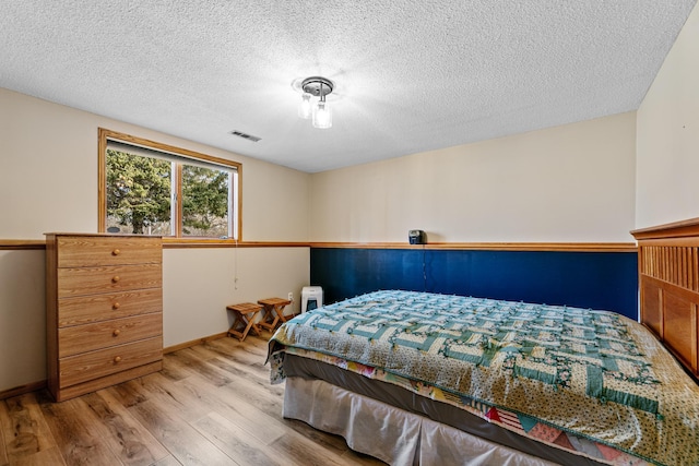 bedroom featuring visible vents, baseboards, a textured ceiling, and wood finished floors