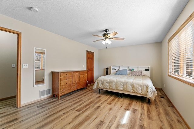 bedroom with visible vents, baseboards, ceiling fan, light wood-style flooring, and a textured ceiling