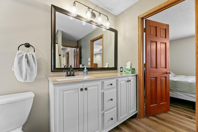 ensuite bathroom with toilet, a textured ceiling, ensuite bath, wood finished floors, and vanity