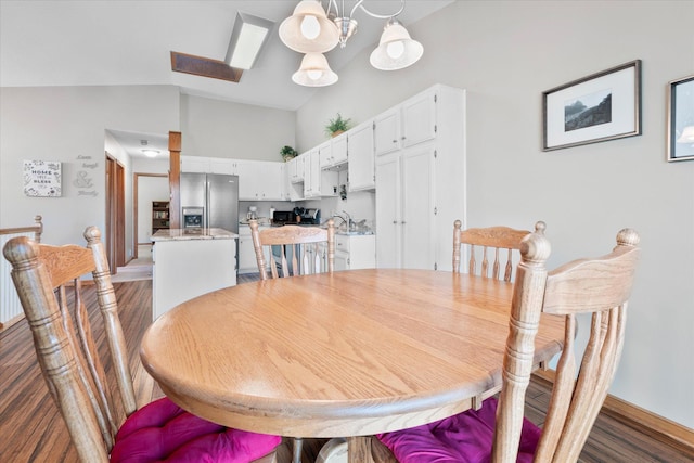 dining area with vaulted ceiling with skylight, a notable chandelier, and wood finished floors