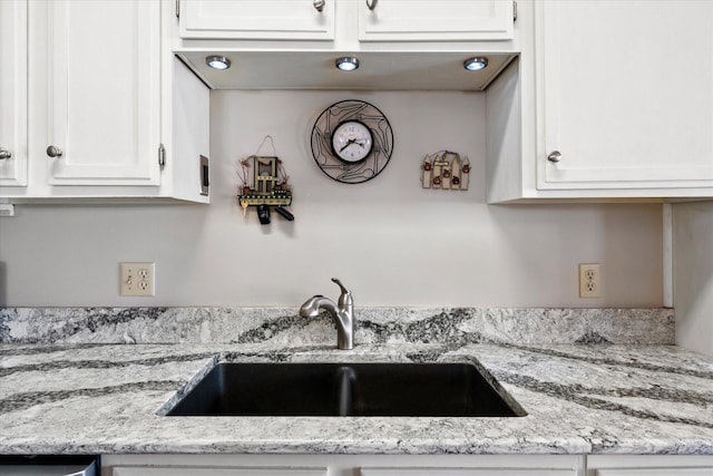 kitchen featuring light stone countertops, white cabinetry, and a sink