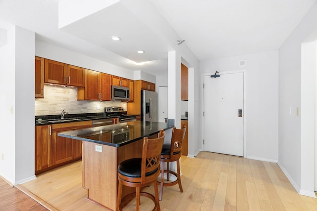 kitchen featuring backsplash, stainless steel appliances, a breakfast bar area, and light wood-style floors