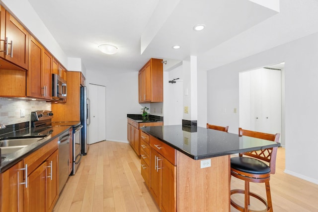 kitchen featuring appliances with stainless steel finishes, light wood-type flooring, a kitchen bar, brown cabinets, and baseboards