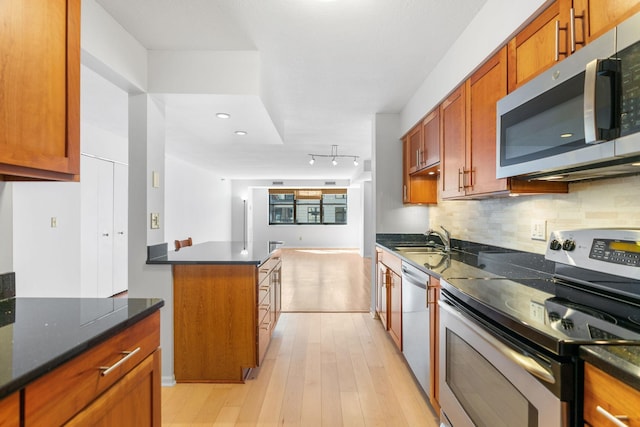 kitchen with stainless steel appliances, a sink, decorative backsplash, light wood-style floors, and brown cabinetry