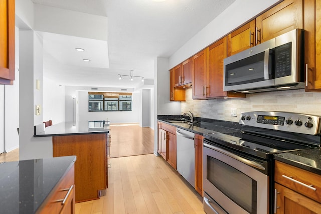 kitchen with stainless steel appliances, a sink, decorative backsplash, light wood-style floors, and brown cabinets
