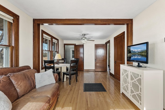 living area with baseboards, light wood-style flooring, and a ceiling fan