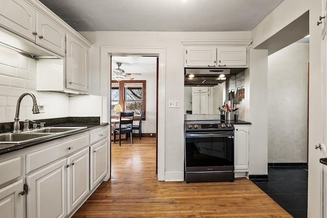 kitchen with electric stove, a sink, under cabinet range hood, dark countertops, and white cabinetry