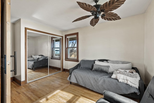 bedroom with a closet, baseboards, light wood-style floors, and a ceiling fan