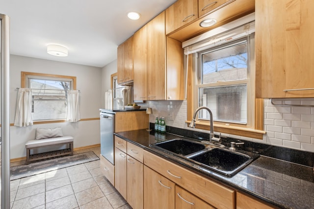 kitchen featuring baseboards, dark stone counters, light tile patterned floors, decorative backsplash, and a sink