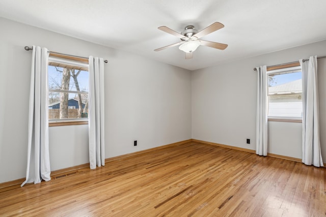 empty room with baseboards, a ceiling fan, visible vents, and light wood-type flooring