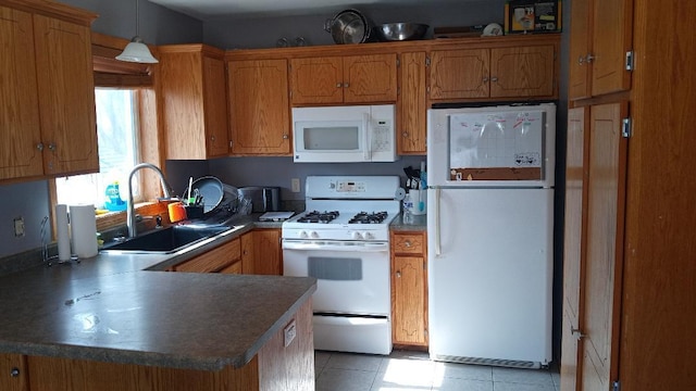 kitchen featuring white appliances, brown cabinetry, a peninsula, and a sink