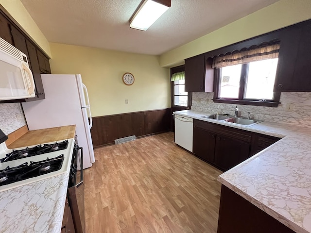 kitchen featuring a wainscoted wall, visible vents, a sink, white appliances, and light countertops