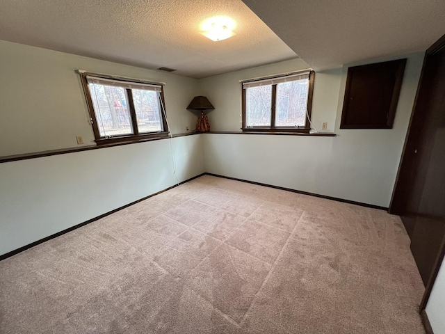 empty room featuring light carpet, visible vents, a healthy amount of sunlight, and a textured ceiling