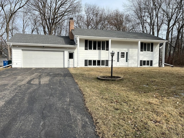 bi-level home featuring a shingled roof, aphalt driveway, a front yard, a chimney, and a garage