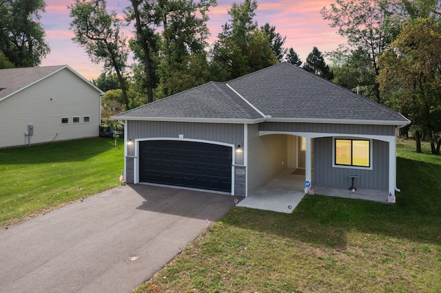 view of front facade featuring a yard, aphalt driveway, a garage, and roof with shingles