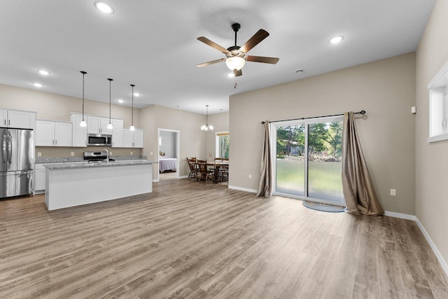 kitchen featuring light wood finished floors, an island with sink, stainless steel appliances, white cabinets, and ceiling fan with notable chandelier