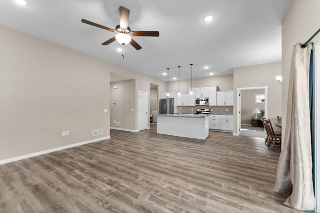 kitchen featuring visible vents, an island with sink, ceiling fan, stainless steel appliances, and open floor plan