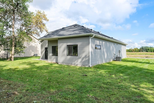 rear view of house with central air condition unit and a lawn