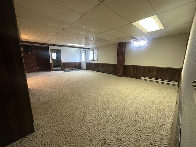 below grade area with a baseboard heating unit, carpet, wood walls, wainscoting, and a paneled ceiling