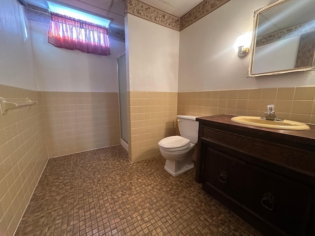 full bath featuring vanity, wainscoting, walk in shower, tile walls, and toilet