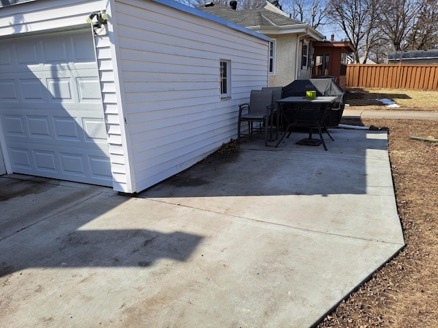 view of patio featuring a garage, concrete driveway, and fence