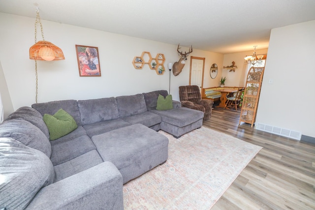 living room featuring an inviting chandelier, wood finished floors, visible vents, and baseboards