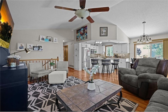 living room with lofted ceiling, a textured ceiling, light wood-style flooring, and ceiling fan with notable chandelier