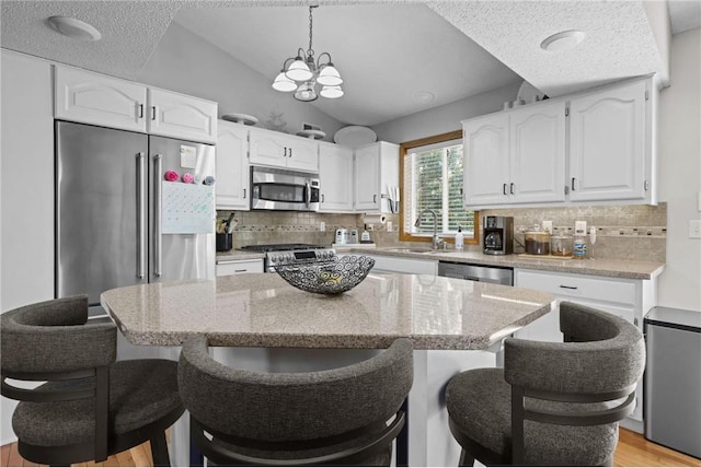 kitchen featuring lofted ceiling, a kitchen breakfast bar, appliances with stainless steel finishes, white cabinets, and a sink