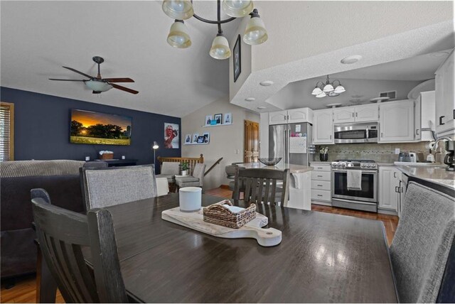 dining area with vaulted ceiling, wood finished floors, ceiling fan with notable chandelier, and visible vents