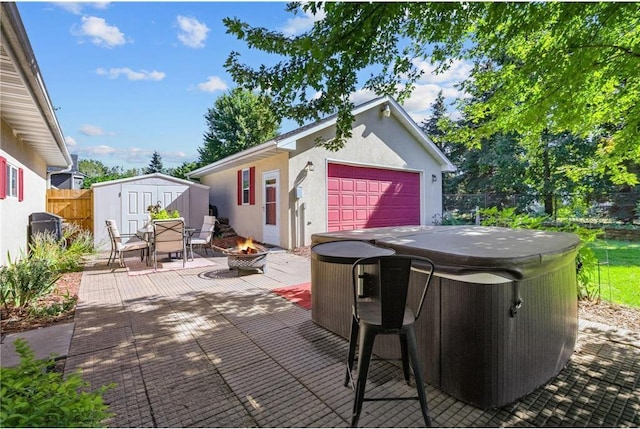 view of patio / terrace featuring a fenced backyard, an outdoor fire pit, an outdoor structure, a garage, and a hot tub