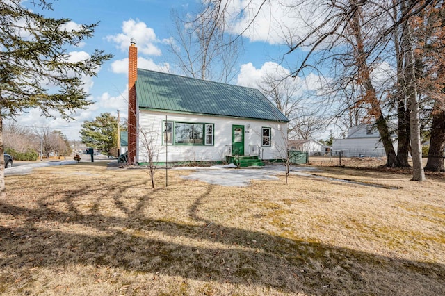 view of front facade with metal roof, a front yard, a chimney, and fence