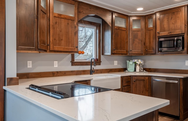 kitchen featuring a sink, stainless steel appliances, light stone countertops, and glass insert cabinets