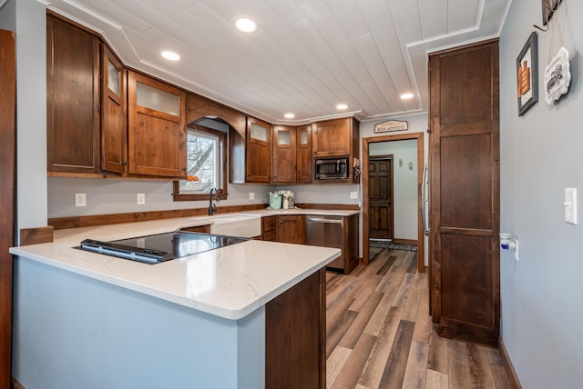 kitchen featuring light wood-type flooring, a sink, stainless steel appliances, a peninsula, and glass insert cabinets