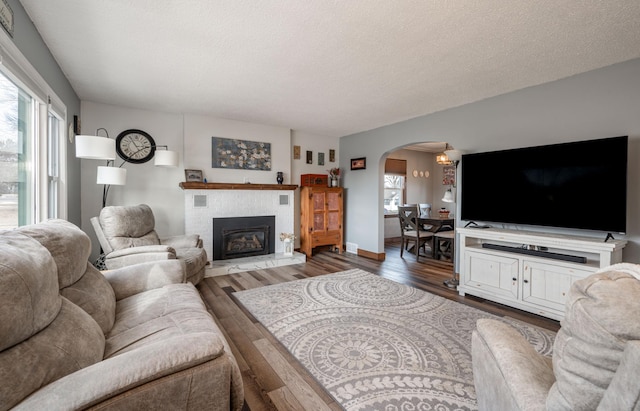 living area with a brick fireplace, wood finished floors, arched walkways, and a textured ceiling