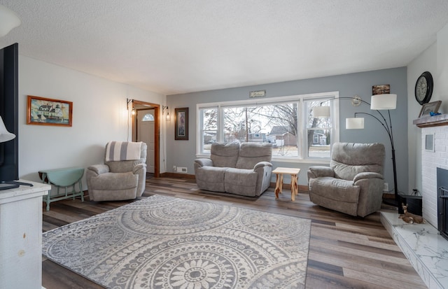 living room with wood finished floors, a fireplace, baseboards, and a textured ceiling