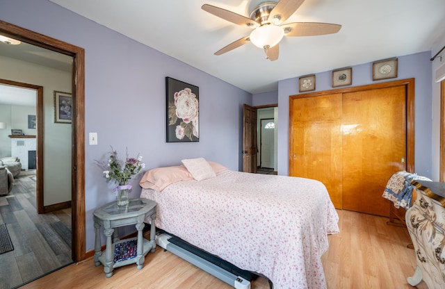 bedroom with ceiling fan, baseboards, light wood-type flooring, a fireplace, and a closet