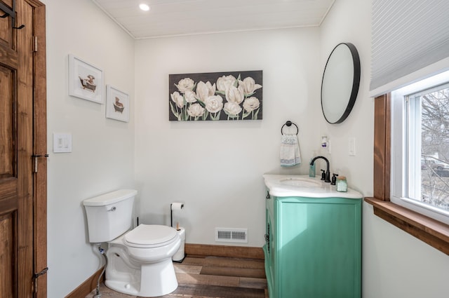 half bathroom featuring vanity, toilet, baseboards, and visible vents