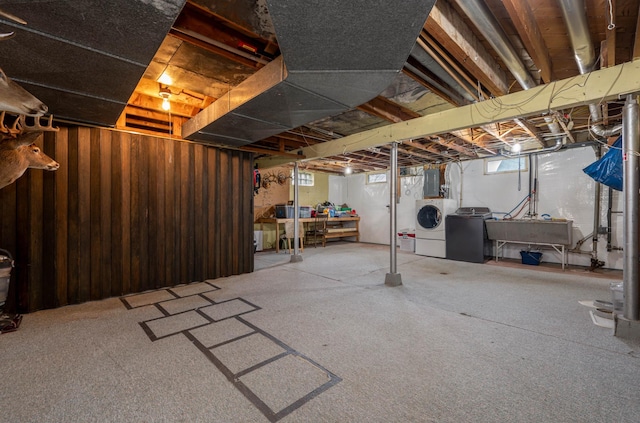 basement featuring a sink, wooden walls, electric panel, and washing machine and clothes dryer