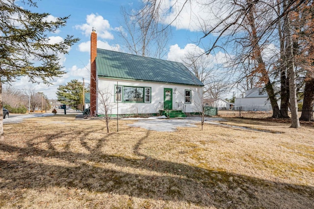 view of front of property featuring metal roof, a front lawn, a chimney, and fence