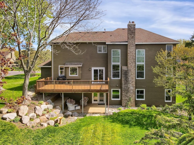 back of property featuring a shingled roof, a wooden deck, a lawn, a chimney, and a patio area